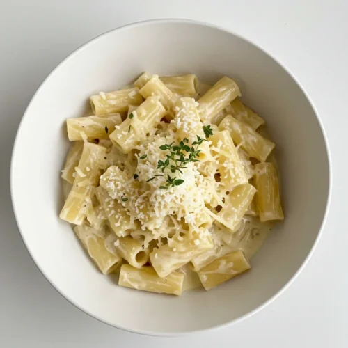 Creamy pasta topped with parmesan and herbs in a white bowl
